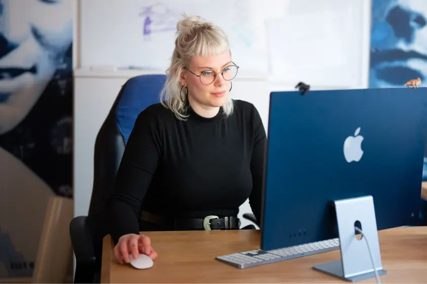 Foto einer Person aus dem Grafikteam an ihrem Arbeitsplatz, frontal vor dem Computerbildschirm.